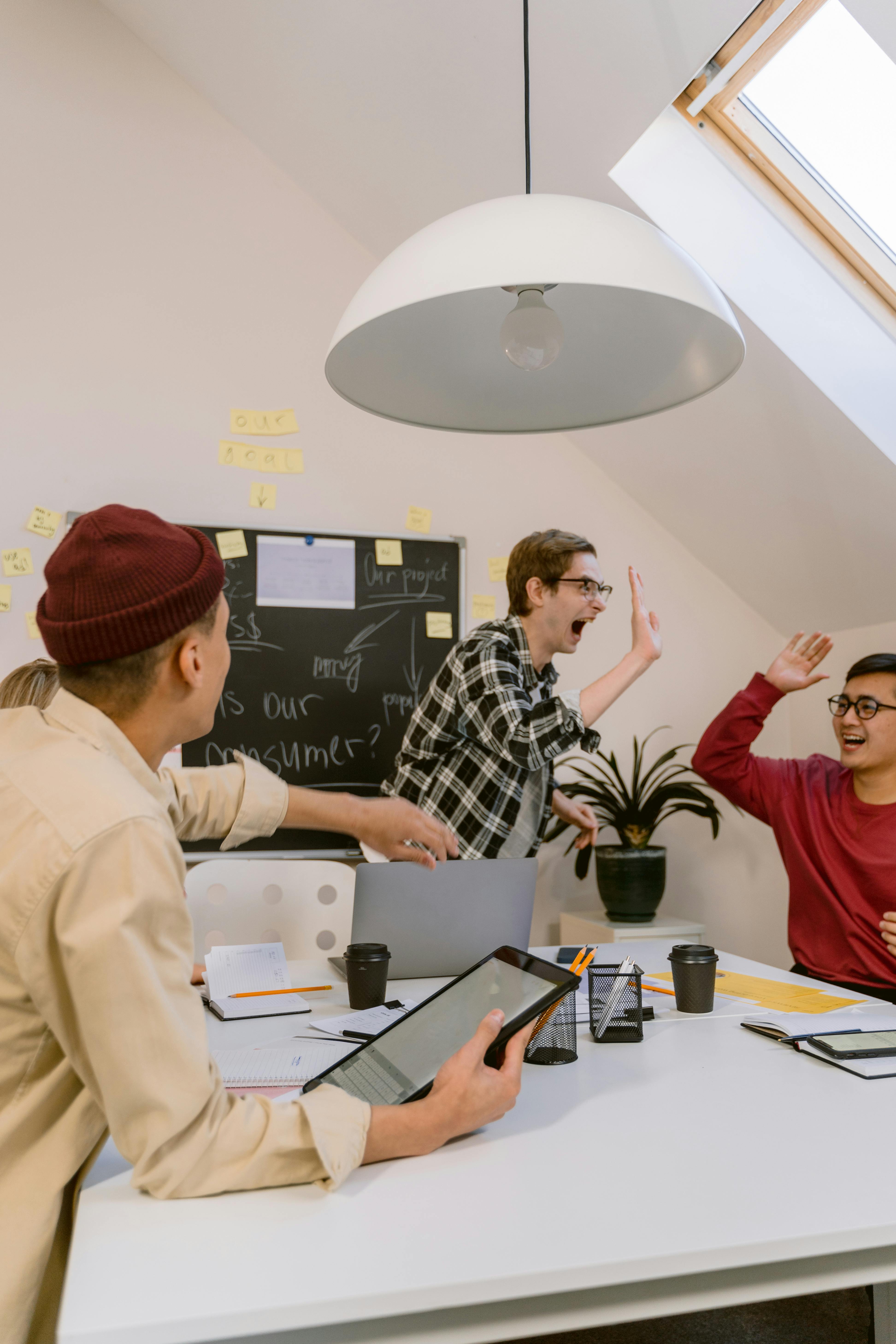 Young professionals in a creative meeting, celebrating teamwork with high-fives in a modern office setting.